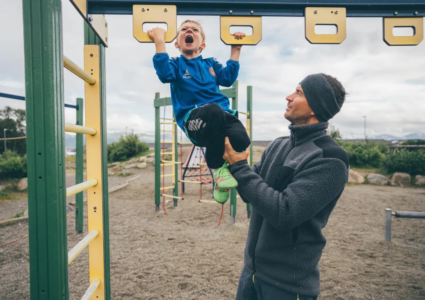 En far løfter barnet sitt i klatrestativet